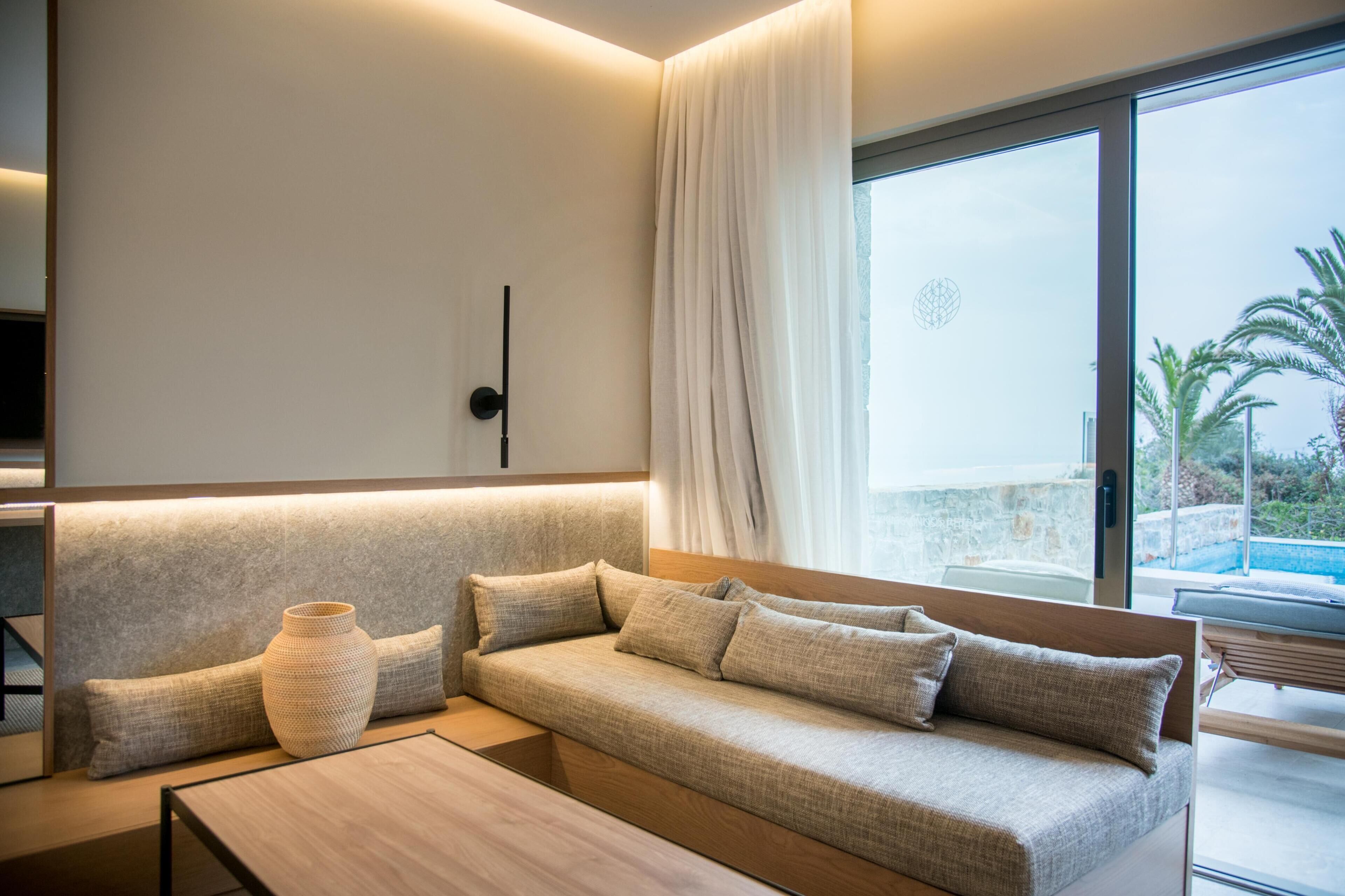 A modern living room with a sofa, a coffee table, and a large window with a view of a pool and palm trees.