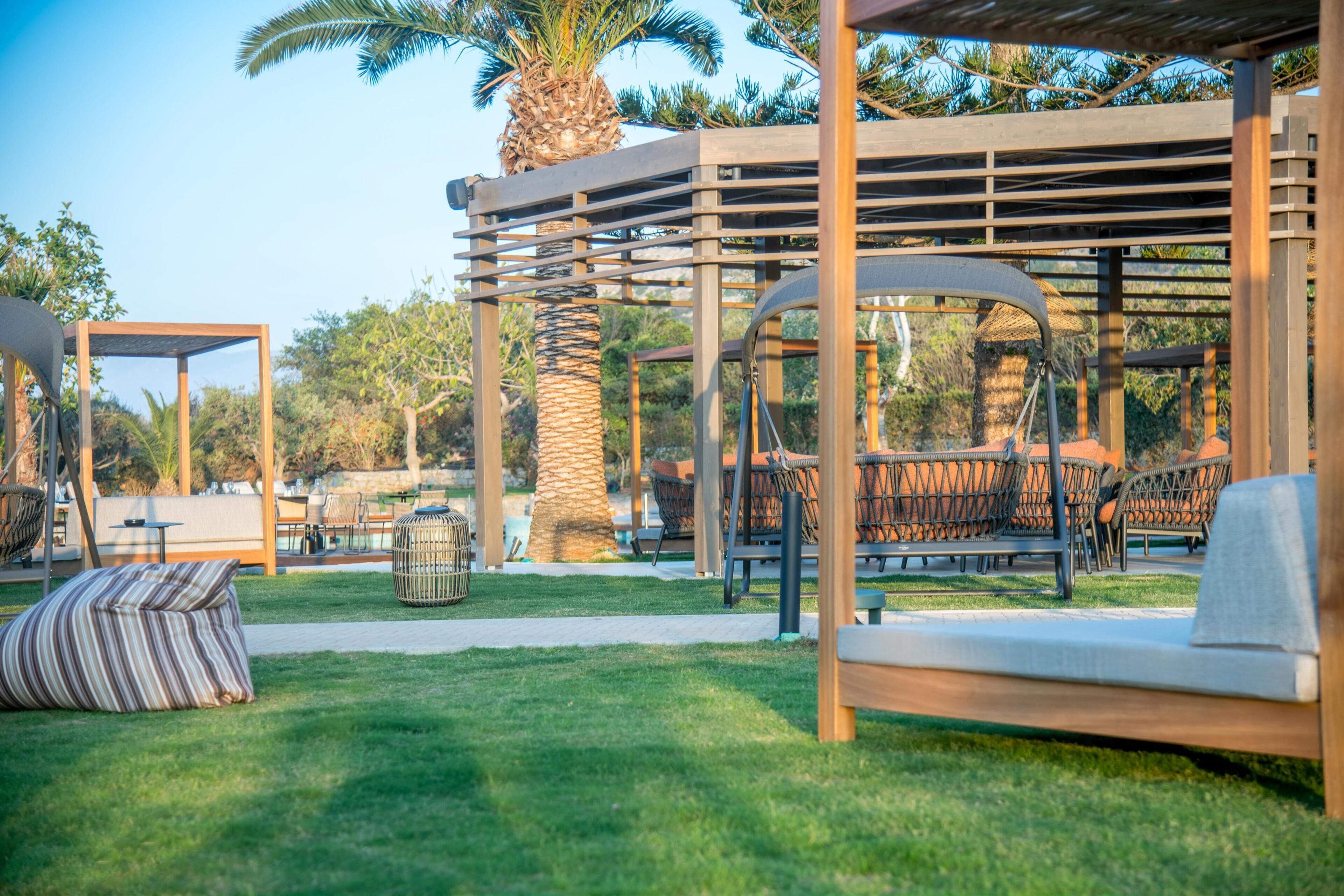 Een buitenruimte met houten pergola’s, comfortabele zitplaatsen en een palmboom.