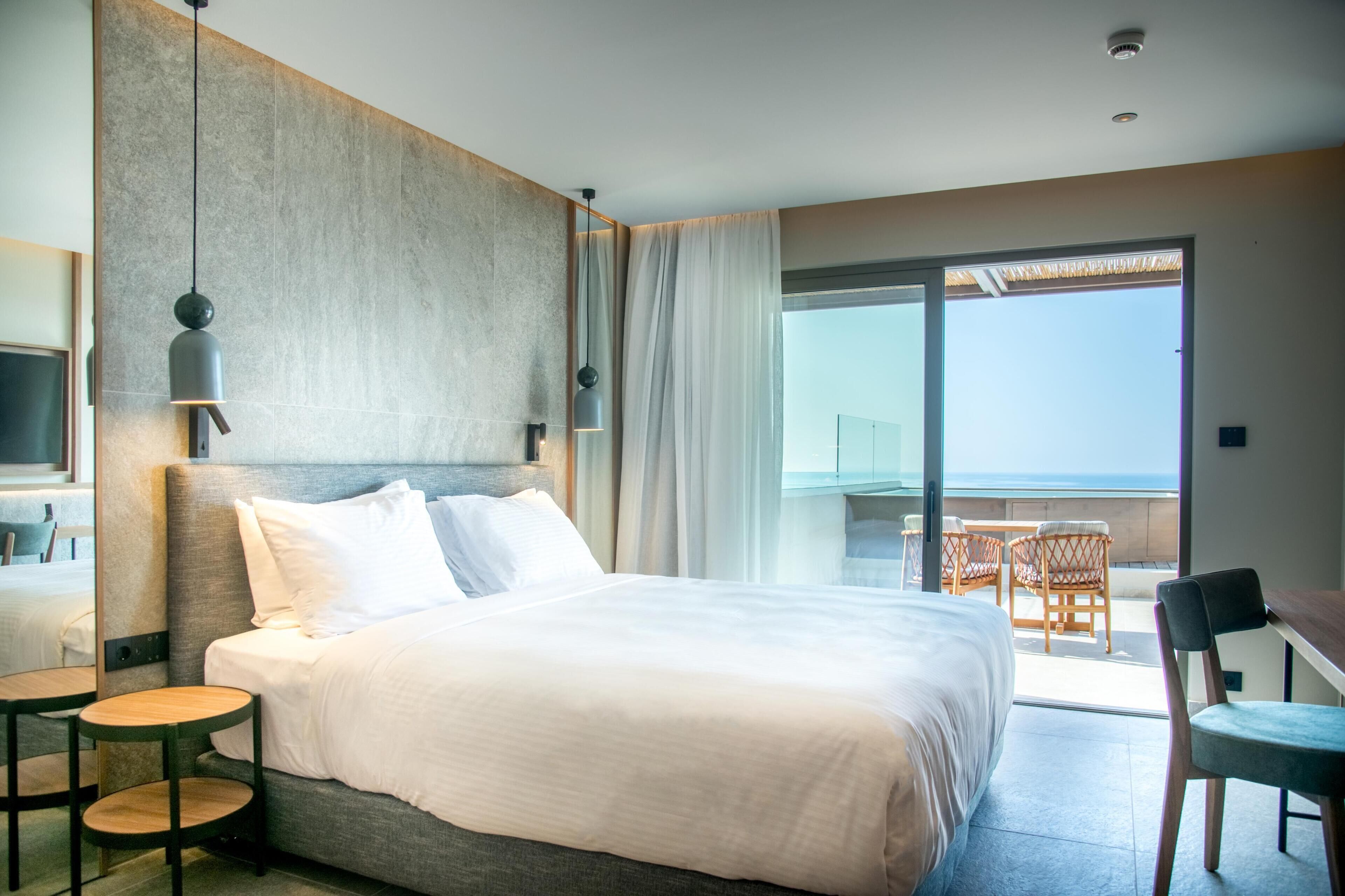 Habitación de hotel con una cama grande, televisión, balcón con mesa y sillas, y vista al mar.