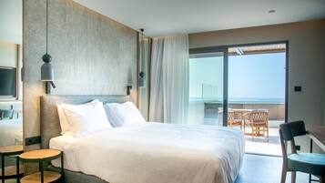 Habitación de hotel con una cama grande, televisión, balcón con mesa y sillas, y vista al mar.