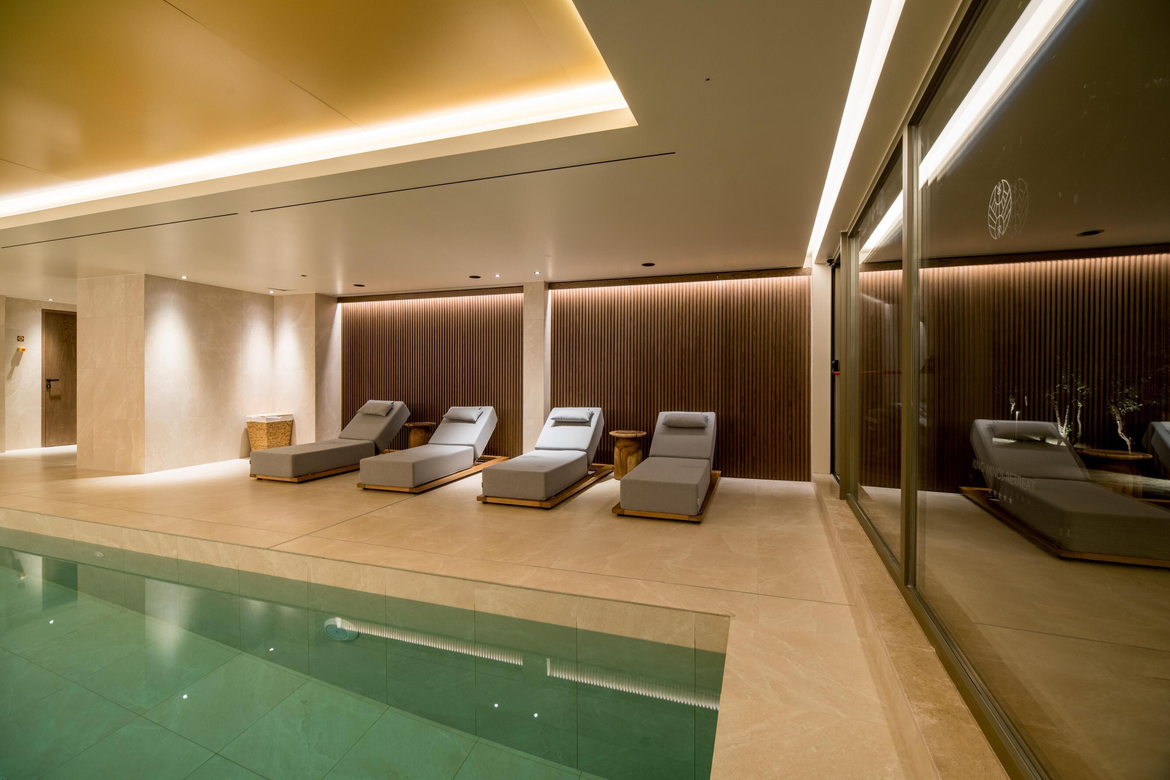Un espace spa moderne doté d’une piscine, de chaises longues et d’un mur en verre.