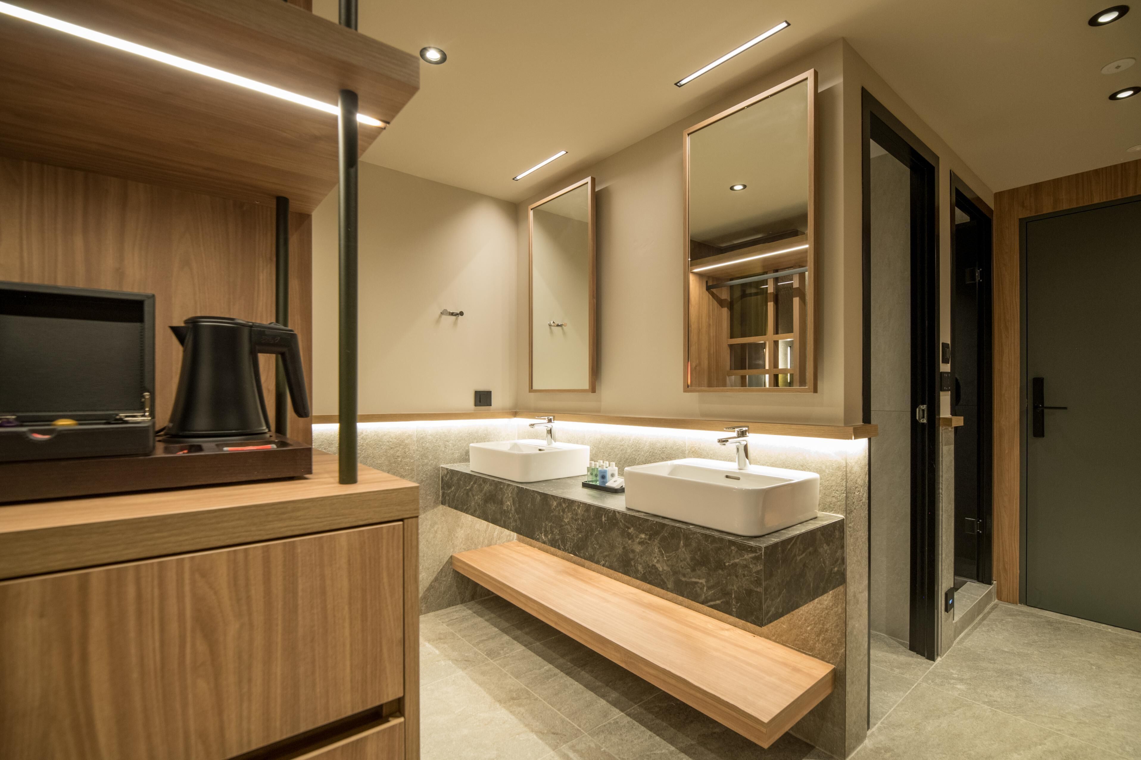 Un baño moderno con muebles de madera, un banco, dos lavamanos y un espejo grande.