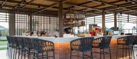 An outdoor bar area with a long counter, multiple bar stools, and a variety of bottles and glasses on shelves.
