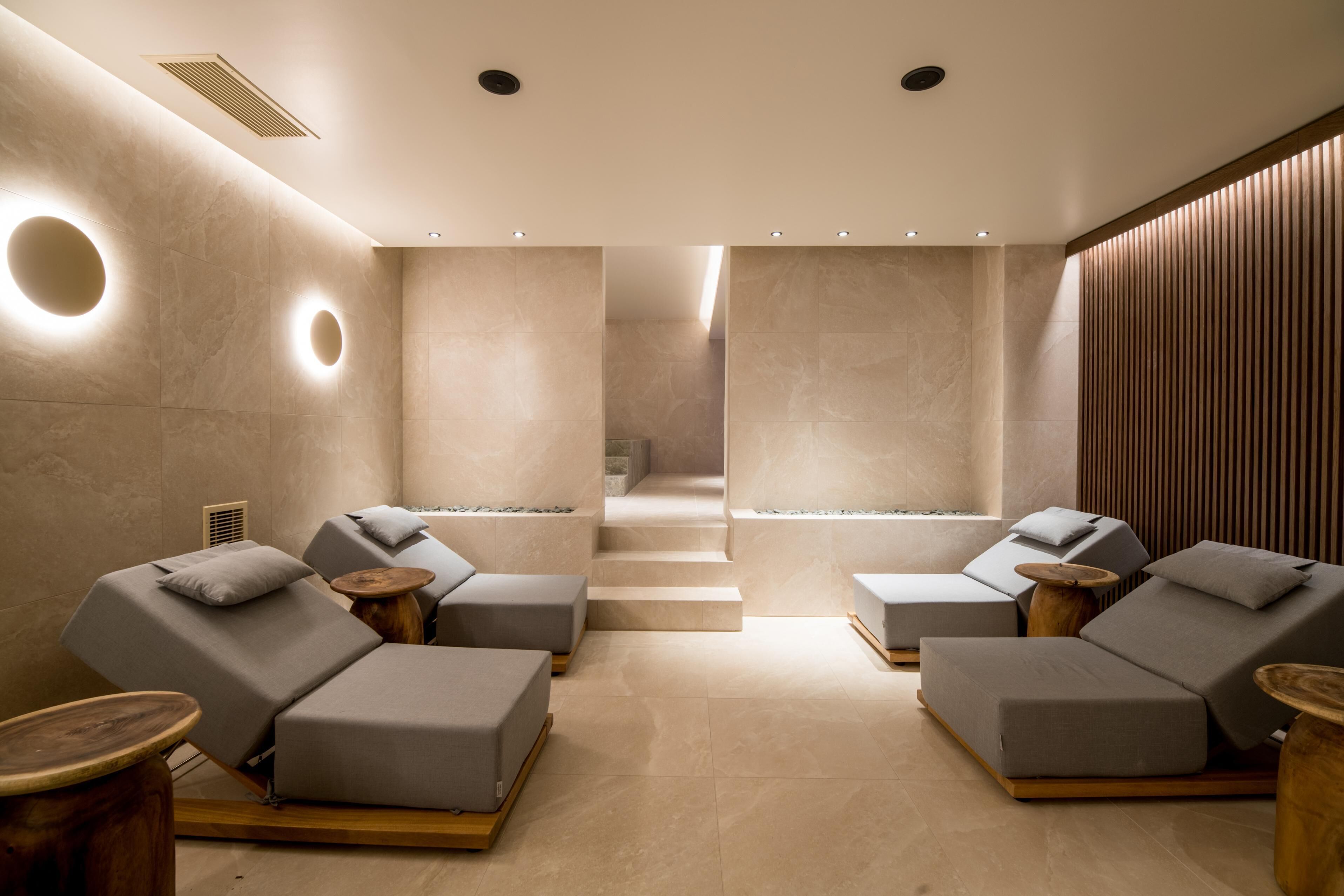 A spa room with two reclining chairs, a wooden floor, and a wall with a circular light fixture.