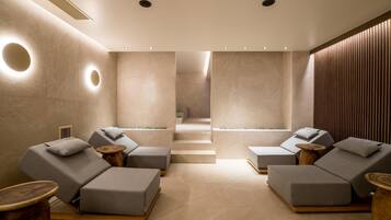 A spa room with two reclining chairs, a wooden floor, and a wall with a circular light fixture.