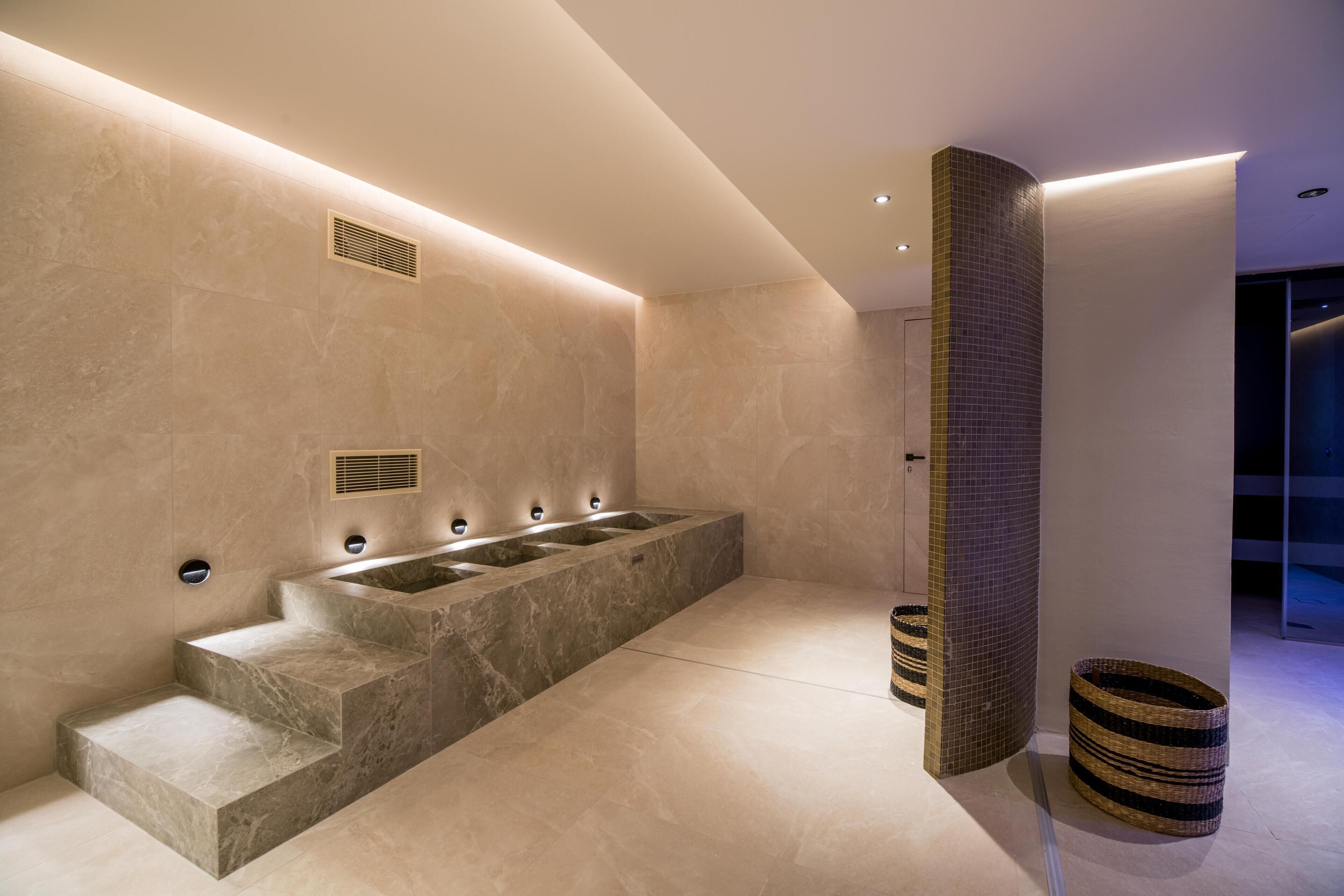 Un baño moderno con un lavamanos grande de mármol, escalones integrados y una zona de ducha con azulejos.