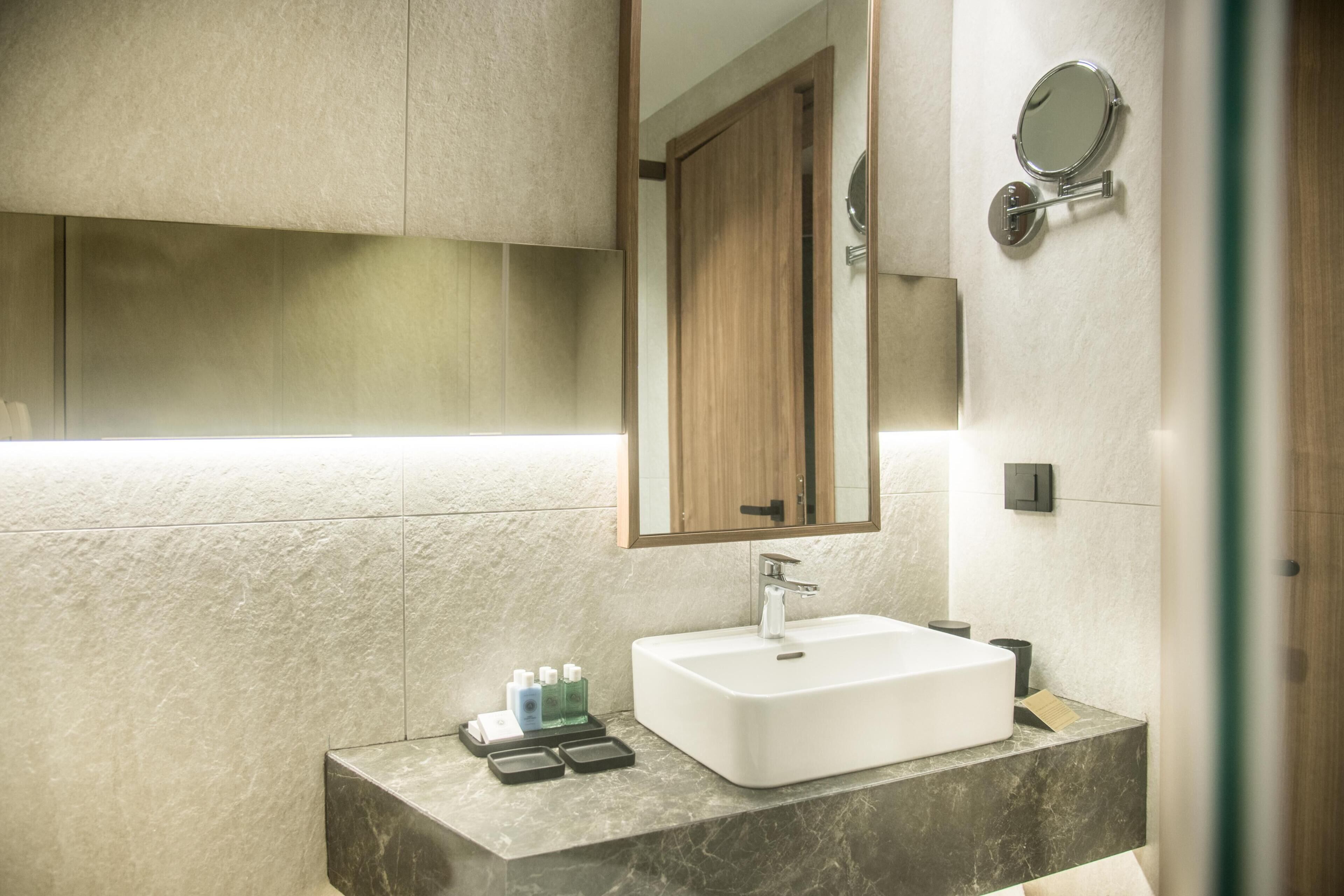 Un baño moderno con un espejo grande, un lavabo blanco y una encimera de mármol.
