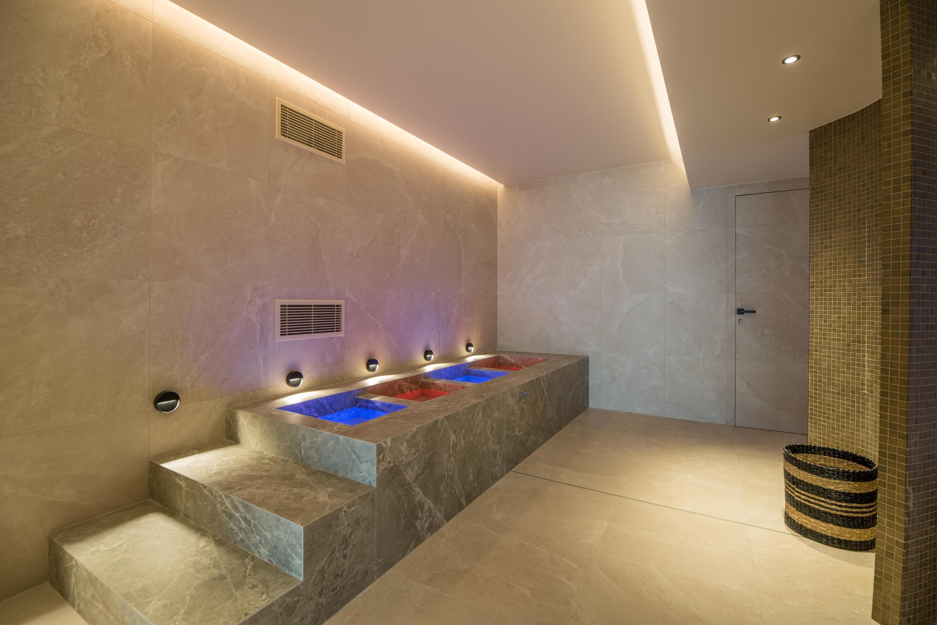 Une salle de bain moderne avec un lavabo en marbre, des marches intégrées et un mur recouvert de carreaux.