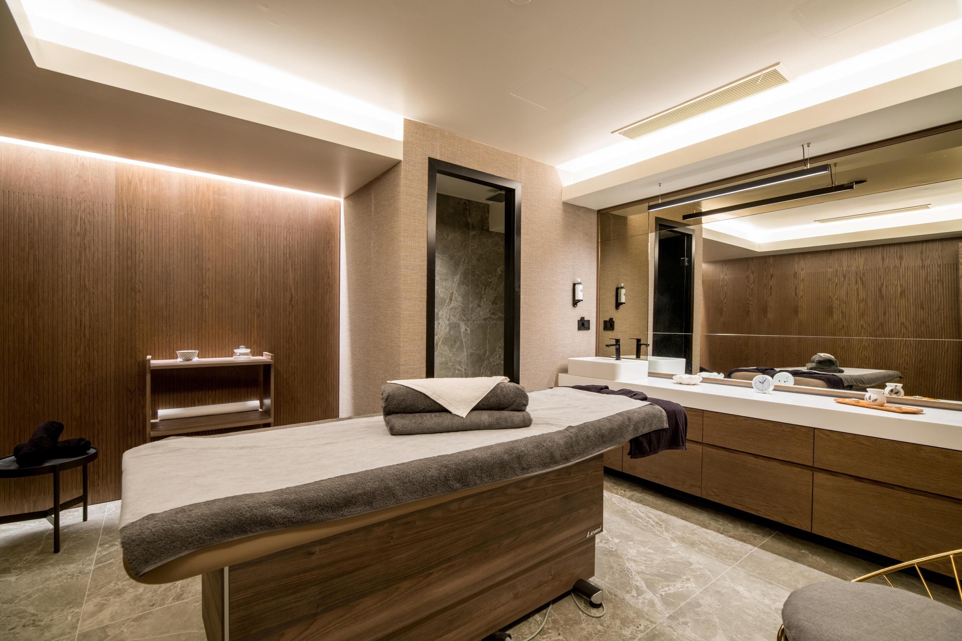 A modern bathroom with a wooden vanity, a large mirror, and a massage table.