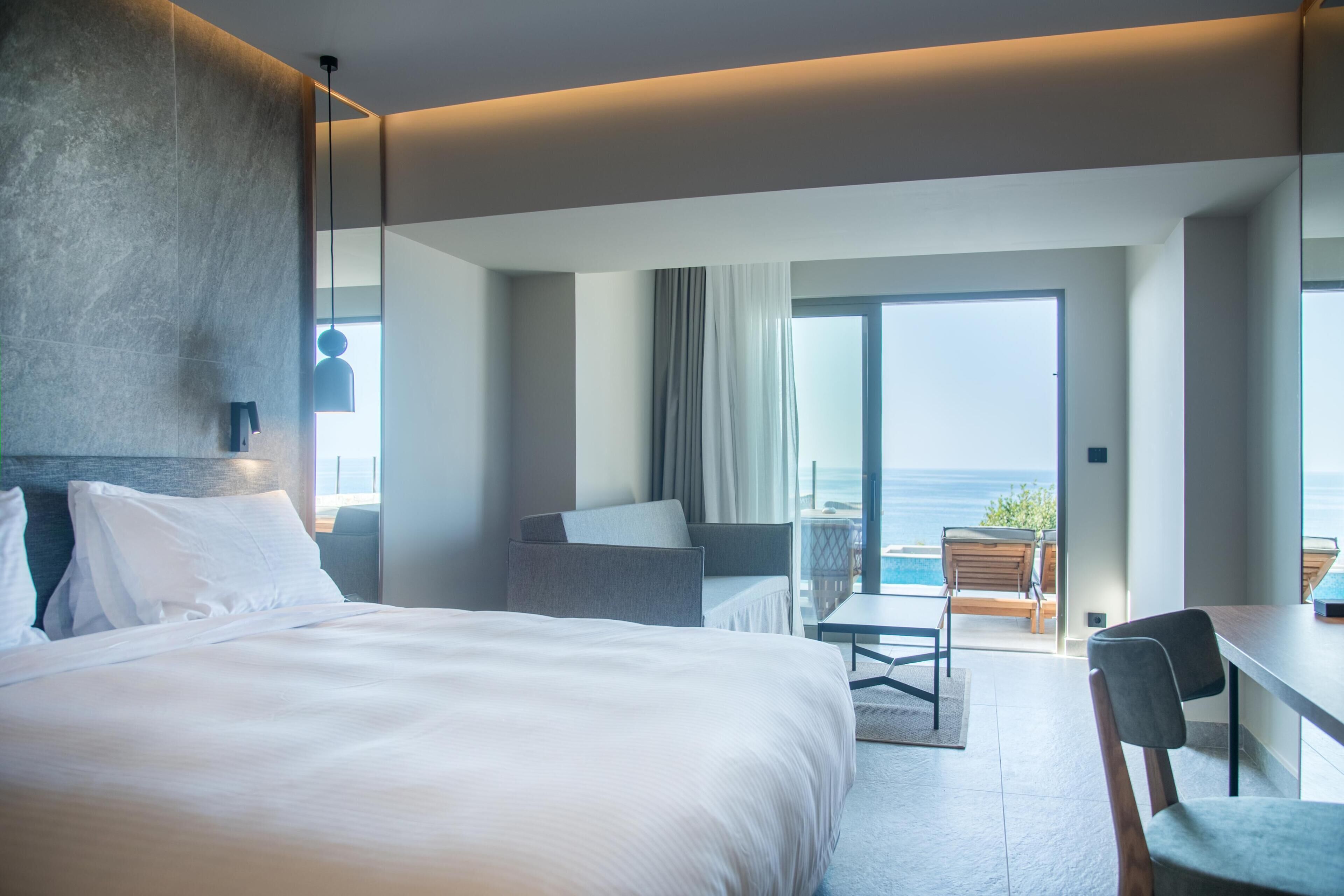 A modern hotel room with a large bed, a desk, and a view of the ocean.