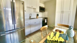 A modern kitchen with stainless steel appliances, white cabinetry, and a glass dining table with a pineapple decoration. - Modern 2BR w/Diamond Head view, beach, FREE parking, king bed, pool, gym,& more! (Honolulu)