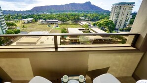 A balcony with a table set for two, overlooking a cityscape with buildings and a mountain. - Modern 2BR w/Diamond Head view, beach, FREE parking, king bed, pool, gym,& more! (Honolulu)