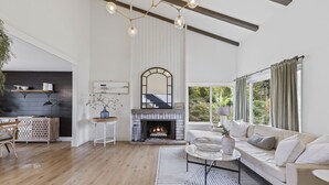 A spacious living room with a fireplace, a sofa, a coffee table, and a dining area with a wooden cabinet. - Stunning Home with Hot Tub, Golf Course Views & Close to all So Cal Attractions! (Mission Viejo)
