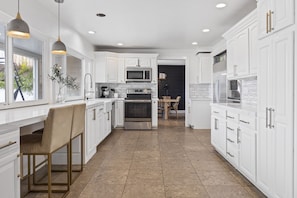 Enjoy cooking in this well-lit kitchen with a central island and bar stool, featuring a stainless steel range hood and gold handles.