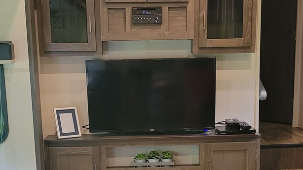 Ein Wohnzimmer mit Flachbildfernseher, Holzschränken, Kamin und Teppichboden.