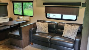 Ein kompaktes Wohnmobil-Interieur mit Essbereich, einer mit gemusterten Kissen ausgestatteten Couch und einem Fenster mit der Aufschrift 'EXIT'.