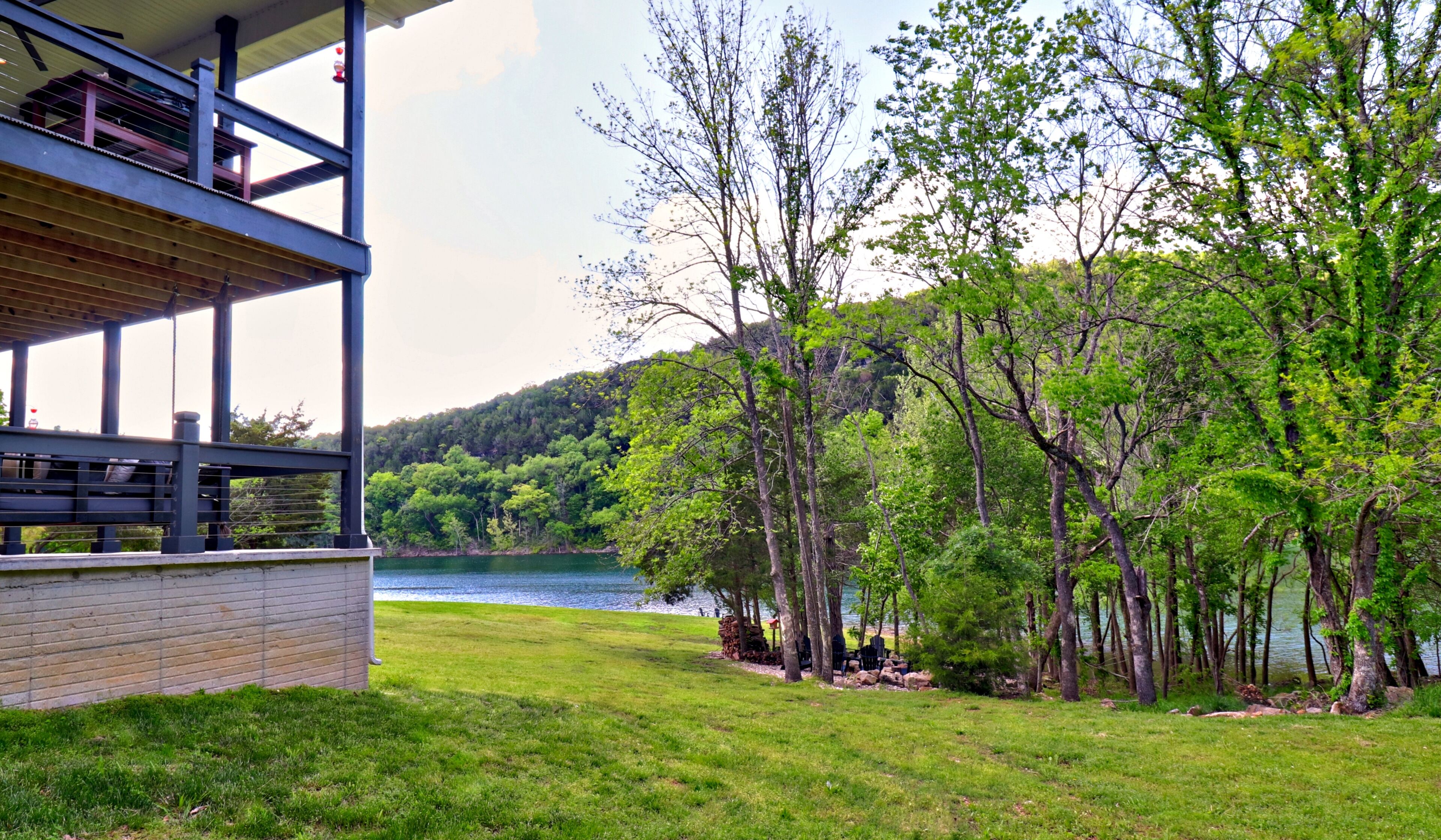 A lakeside property with a wooden deck, a brick wall, and a view of the lake and forested hills.