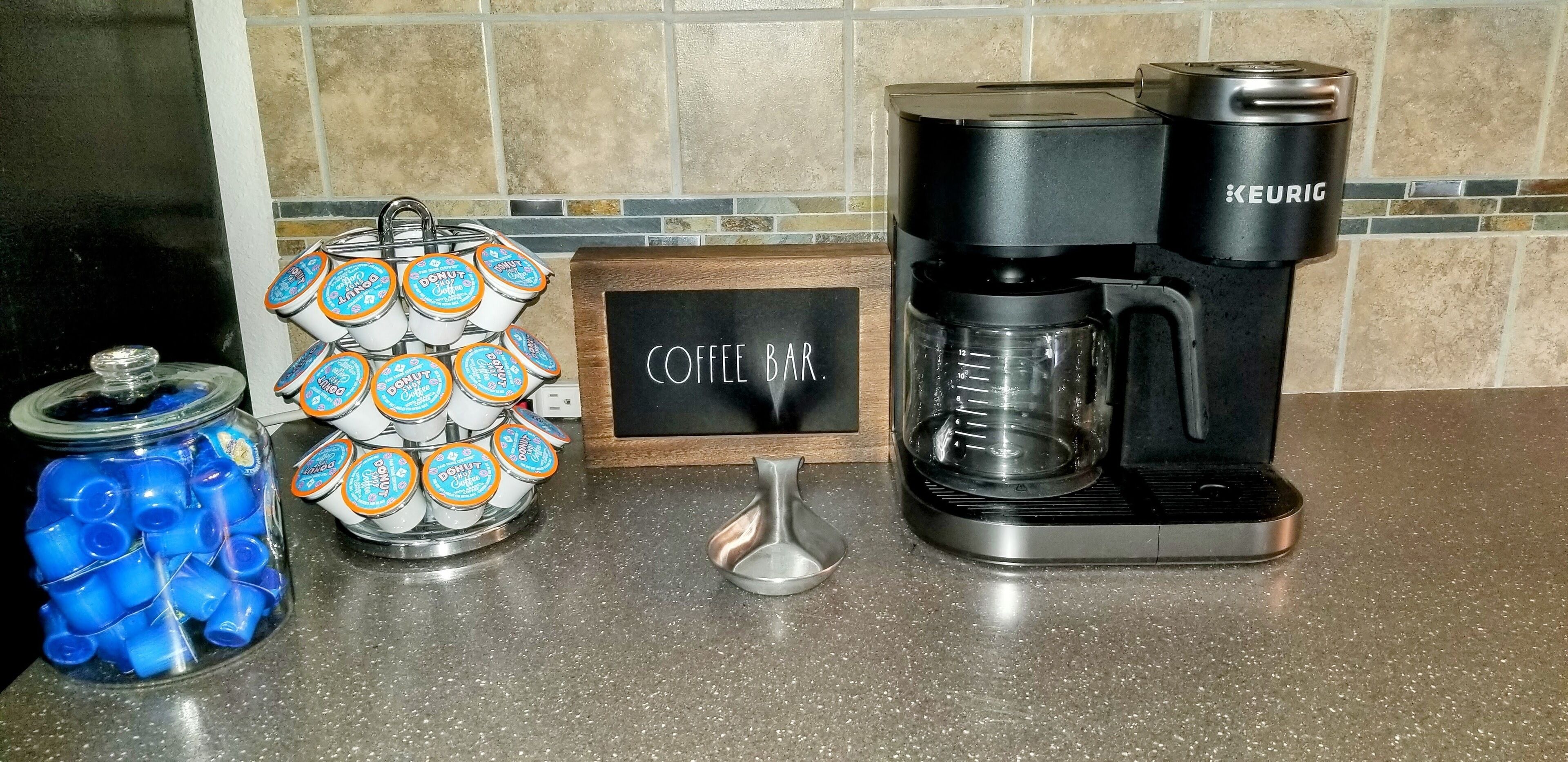 A coffee maker, a jar of blue straws, and a dispenser of donut-shaped containers on a kitchen counter.