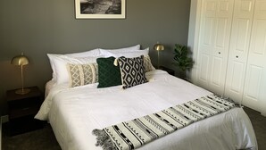 A neatly made bed with white linens, a patterned throw blanket, and several decorative pillows. A framed black and white photograph hangs above the bed.