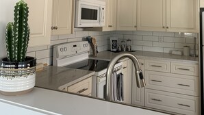 A modern kitchen with white cabinets, a microwave, a stainless steel sink, and a potted cactus.