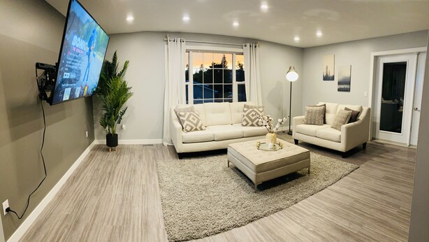 A modern living room with two sofas, a coffee table, a TV mounted on the wall, a potted plant, and a window with curtains.