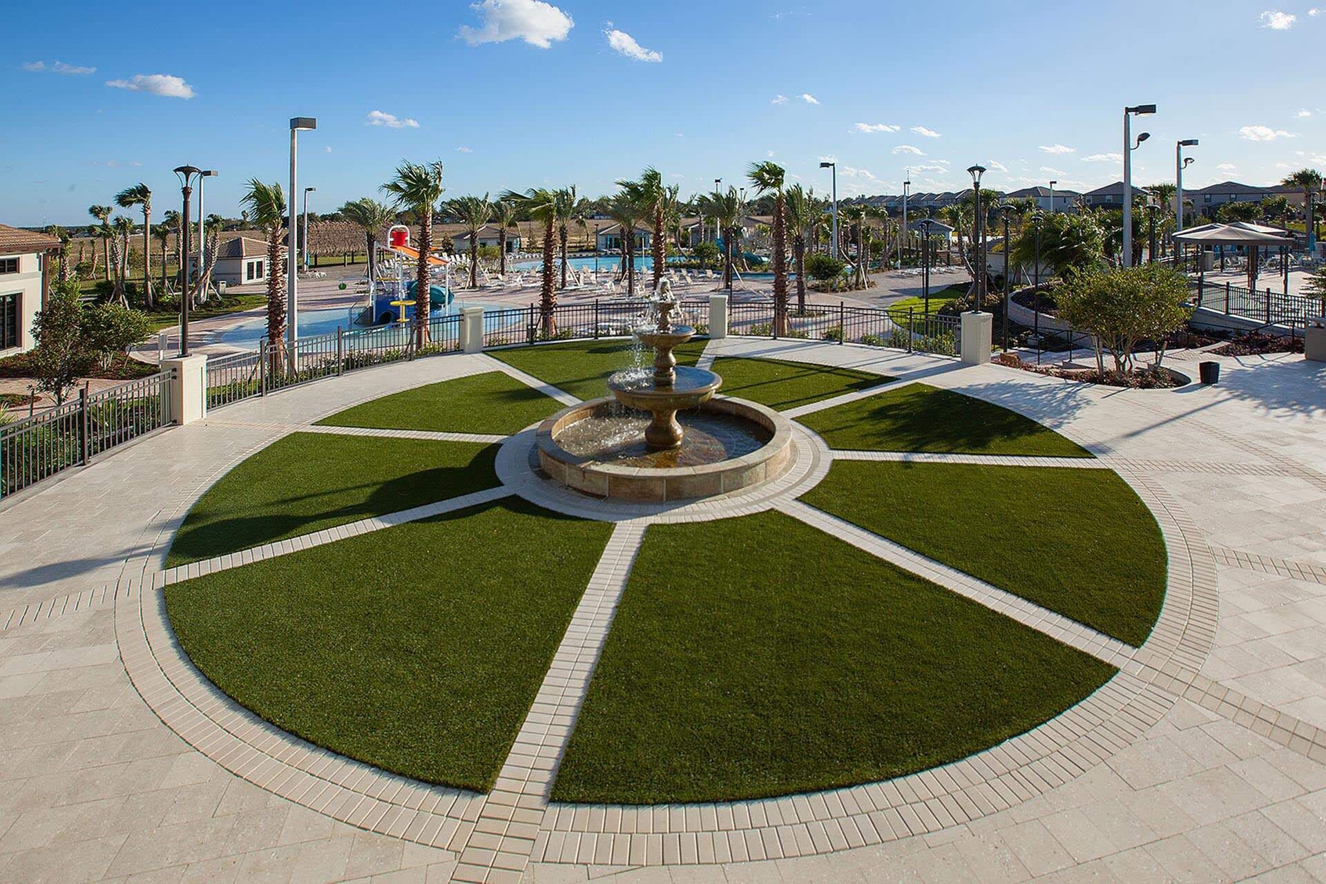 A circular fountain surrounded by a well-maintained lawn with a pool in the background.