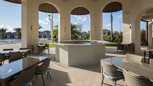An outdoor patio area with a central island, wicker furniture, and views of a pool and palm trees.