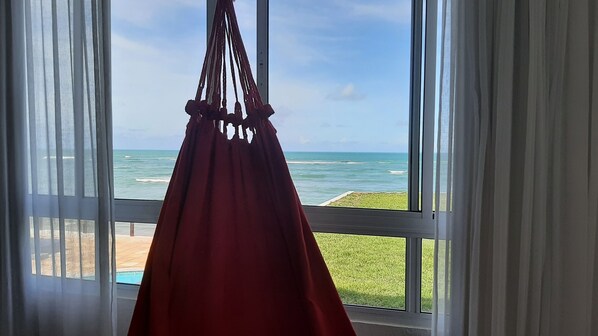 Una hamaca colgada junto a una ventana con vista a la playa.