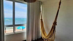 A room with a large window overlooking the ocean, a hammock, and a blue umbrella. - Recanto Há Mar (Maceió)