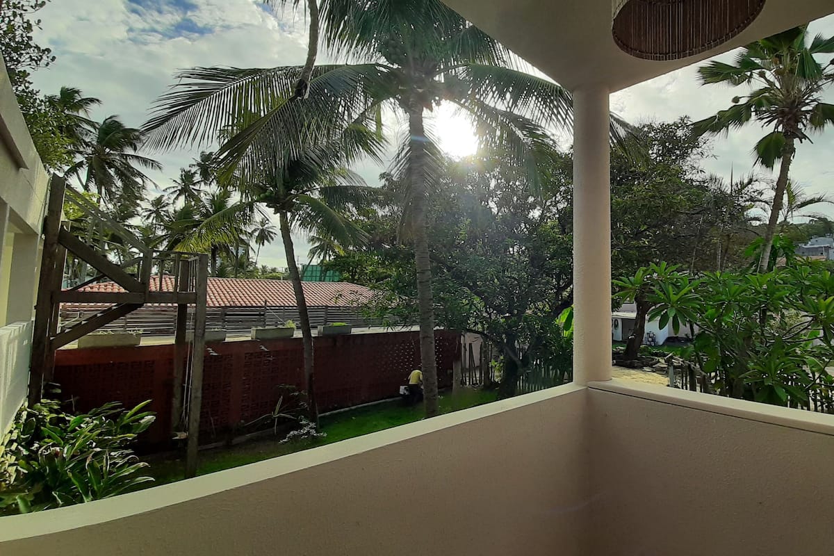 A balcony with a view of a garden, palm trees, and a distant building.