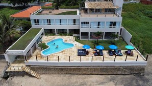 A modern building with a swimming pool, outdoor seating, and a small garden area. - Recanto Há Mar (Maceió)