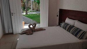 A hotel room with a bed, a wooden headboard, a window with a view of a garden, and a door with a curtain. - Recanto Há Mar (Maceió)
