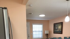 A kitchen with a refrigerator, a dining area with a table and chairs, a window with blinds, a sofa, and a painting on the wall.