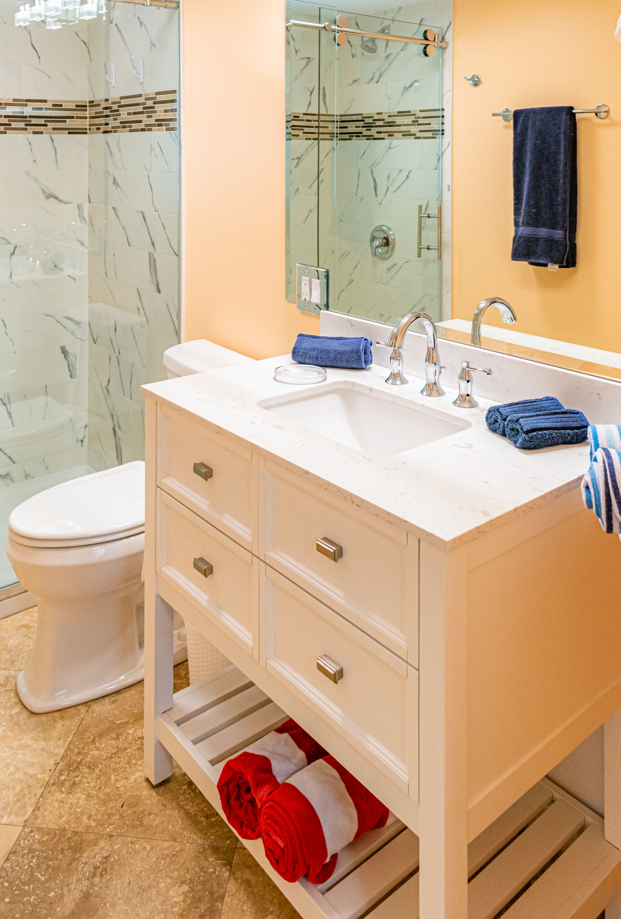 Un baño con tocador blanco, cabina de ducha de vidrio y pared decorada en amarillo.