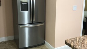 A kitchen with a stainless steel refrigerator, beige walls, and a granite countertop.