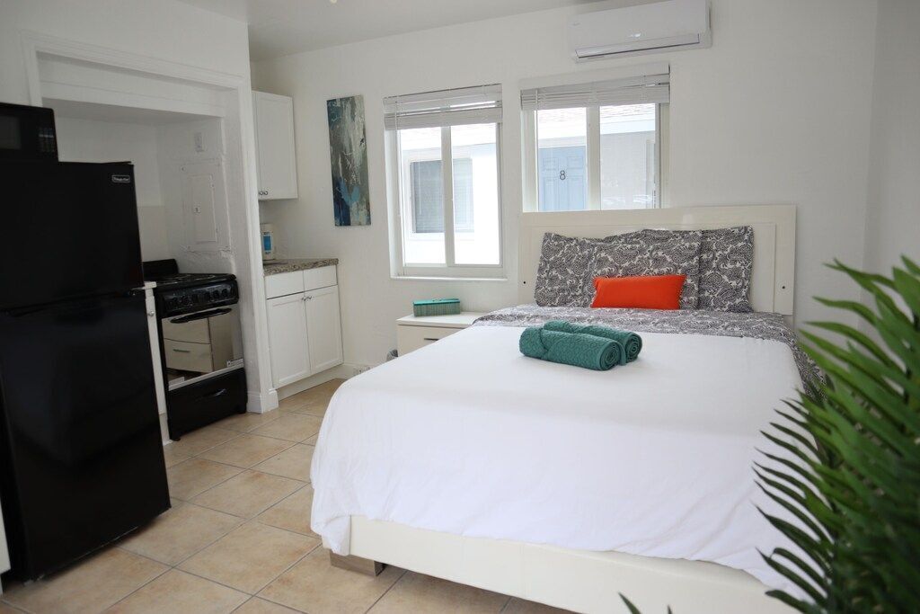 A compact bedroom with a bed, a nightstand, a window, and a kitchenette.