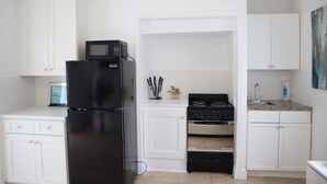 A compact kitchen with white cabinets, a black refrigerator, a stove, and a microwave.