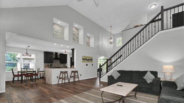 Un vaste espace de vie comprenant un escalier, un coin repas avec une cuisine en arrière-plan, et un canapé gris agrémenté d’une lampe.