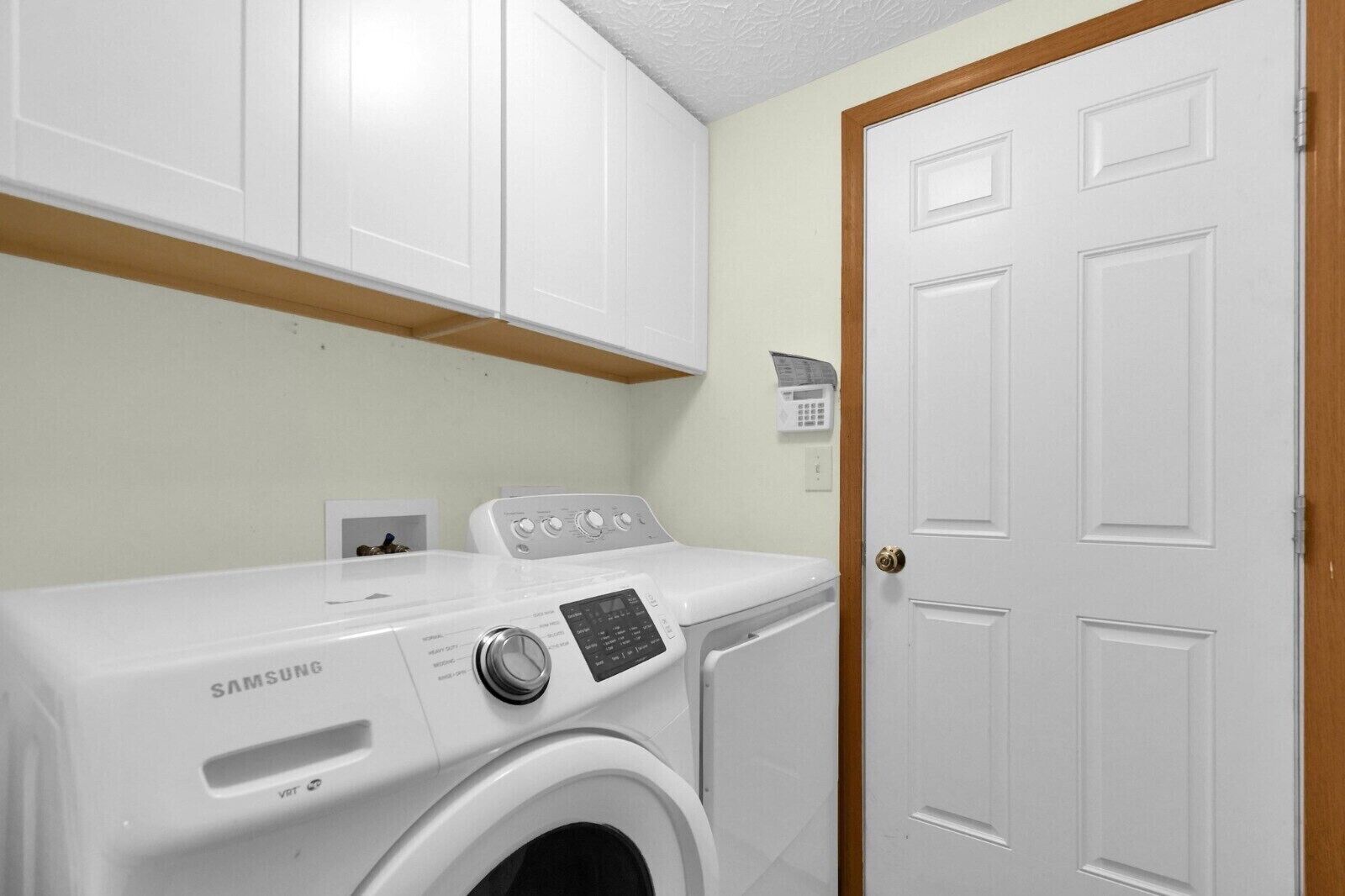 A laundry room with a Samsung washer and dryer, white cabinets, and a wooden door.
