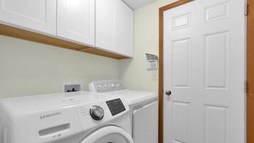 A laundry room with a Samsung washer and dryer, white cabinets, and a wooden door.