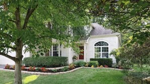 Une maison blanche avec une pelouse bien entretenue et un arbre au premier plan.