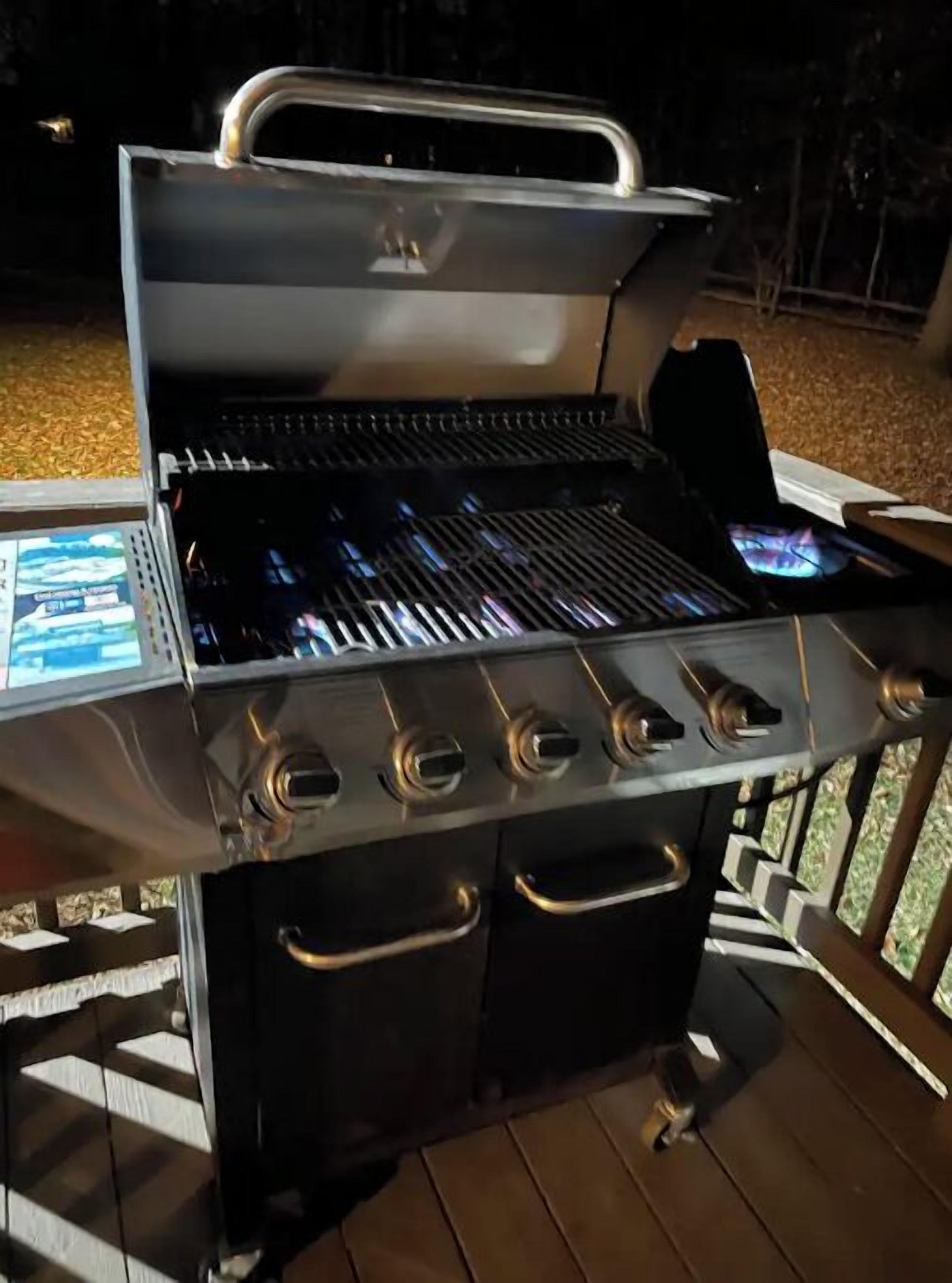 A portable grill with four burners and a digital display, set on a wooden deck.