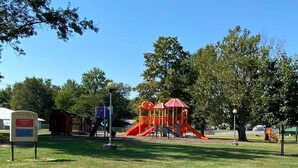 A playground with slides and climbing structures, surrounded by trees and a clear sky. - Comfy Clean & Cute (Marion)