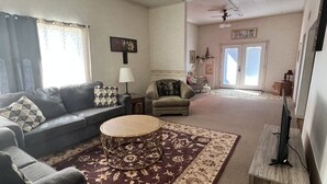 A living room with a sofa, armchair, and a coffee table. There is a television on a stand and a patterned rug on the floor. - Comfy Clean & Cute (Marion)