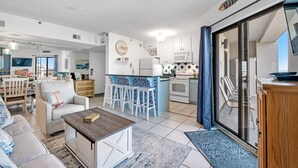A spacious living area with a kitchen, a dining area, and a sliding glass door leading to a balcony. - Gulf Shores Plantation-Dunes 5208 (Gulf Shores)