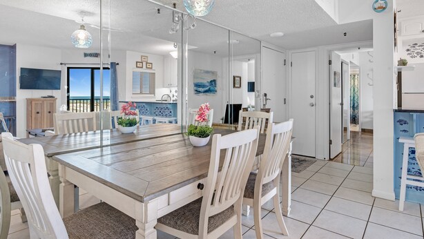 A dining area with a wooden table, white chairs, and a large mirror. - Gulf Shores Plantation-Dunes 5208 (Gulf Shores)