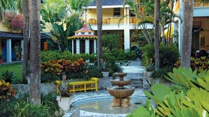 A courtyard with a fountain, yellow bench, and lush greenery. - Newly Remodeled Home with Spacious Backyard! (Fort Lauderdale)