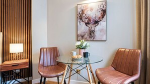 Una habitación moderna con dos sillones de cuero, una mesa de vidrio, una mesita de noche de madera con una lámpara y un cuadro abstracto enmarcado en la pared.