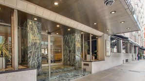 Fachada de hotel de mármol, puertas de cristal y una escalera que lleva al vestíbulo.