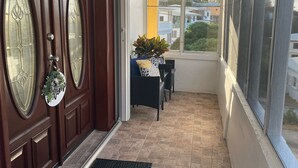 Een overdekt balkon met uitzicht op gebouwen, een houten deur met ruitpanelen en een klein zitgedeelte met een plant.